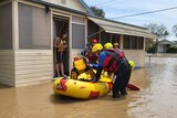 A resident standing in thongs in a door of a house with a dog about to get into a rescue raft in floodwaters with personnel.