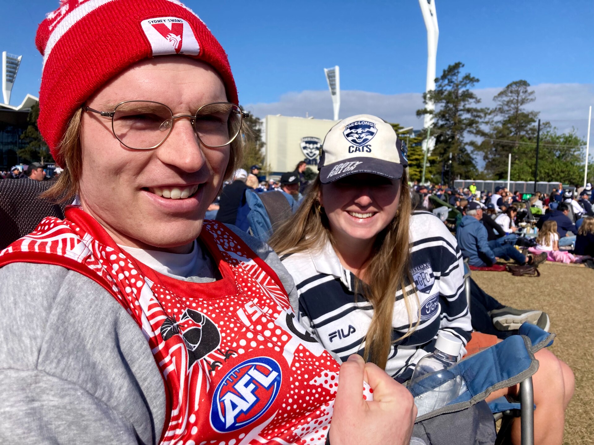 A man in Swans gear and a woman in Cats gear watch a football game.