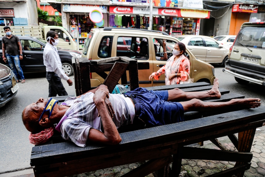 A man wearing a face mask on his chin sleeps by a busy street in Kolkata, India.
