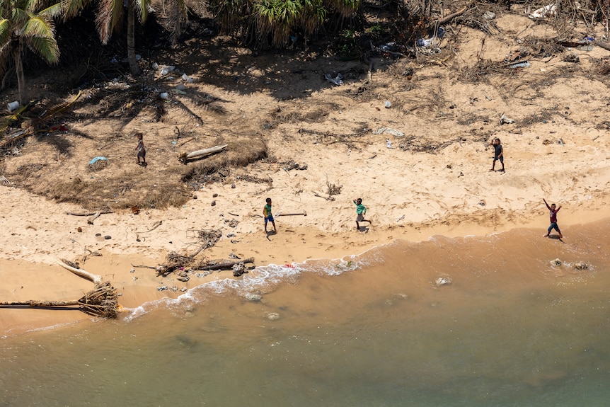  Children play on the beach where debris from damaged building and trees is strewn around.