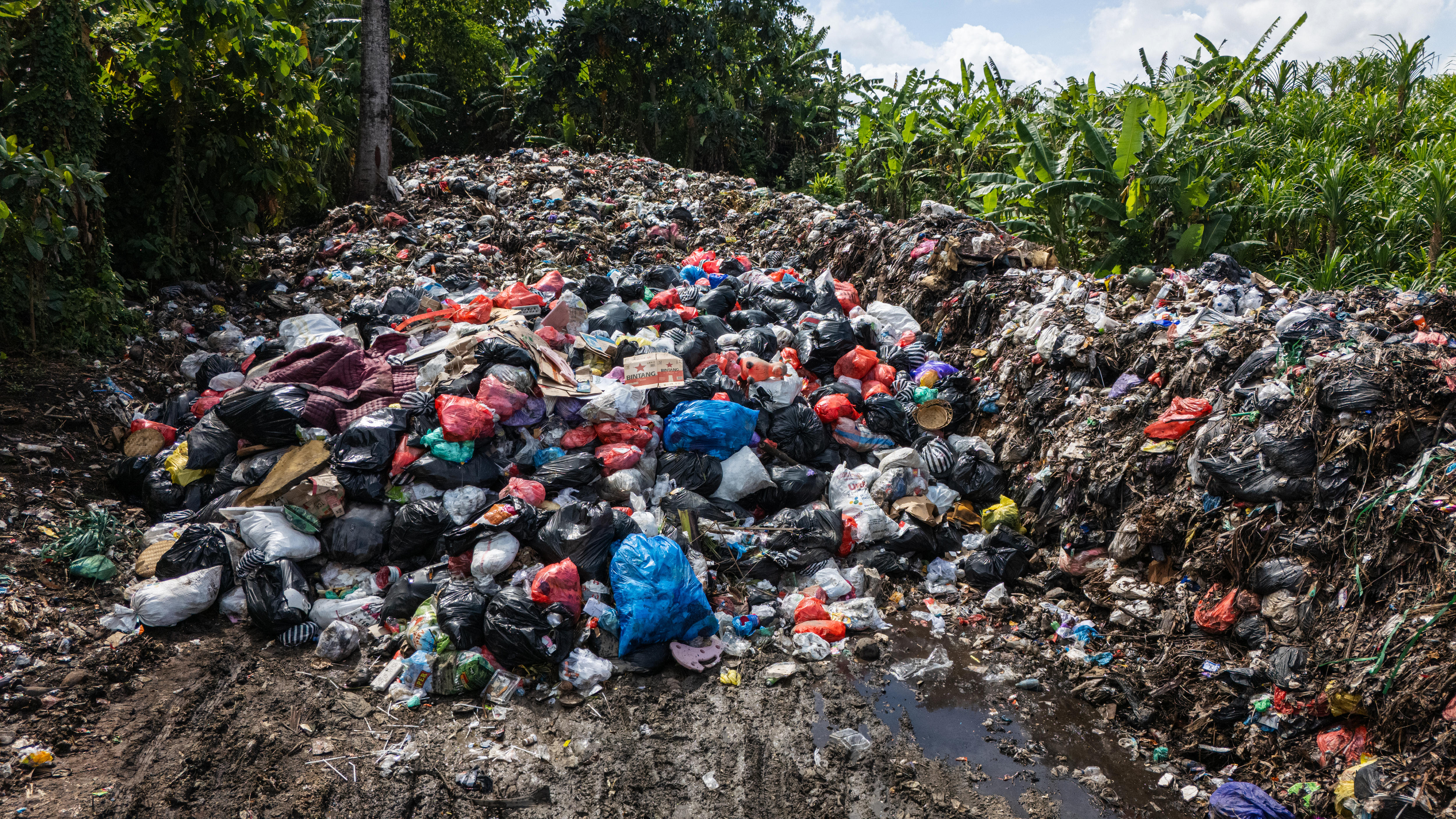 A pile of trash, filled with torn plastic bags, food scraps and plastic bottles, surrounded by dirt.
