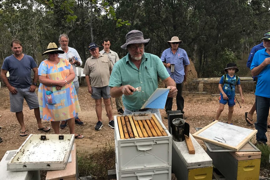 Beekeeper Maurie Damon standing next to a hive, teaching a group of others who stand in the background