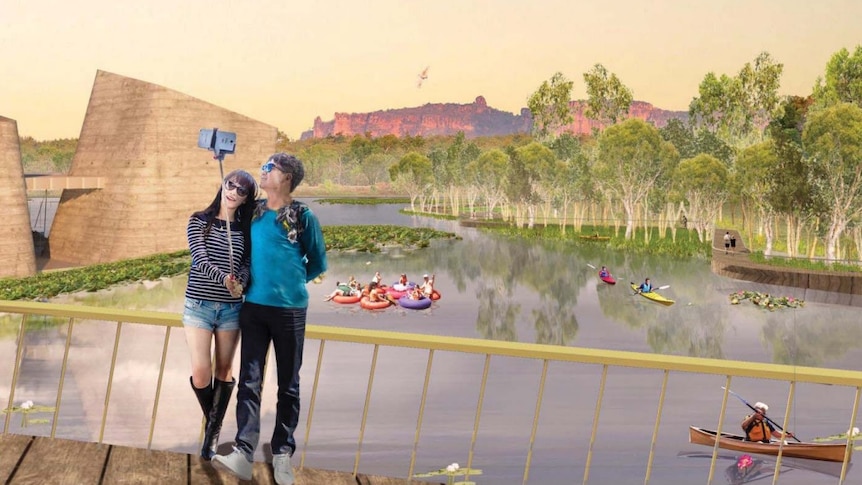 A couple take a picture with a selfie stick, in front of a lake which people are kayaking on