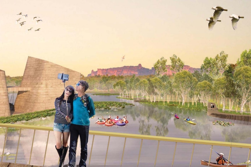 A couple take a picture with a selfie stick, in front of a lake which people are kayaking on