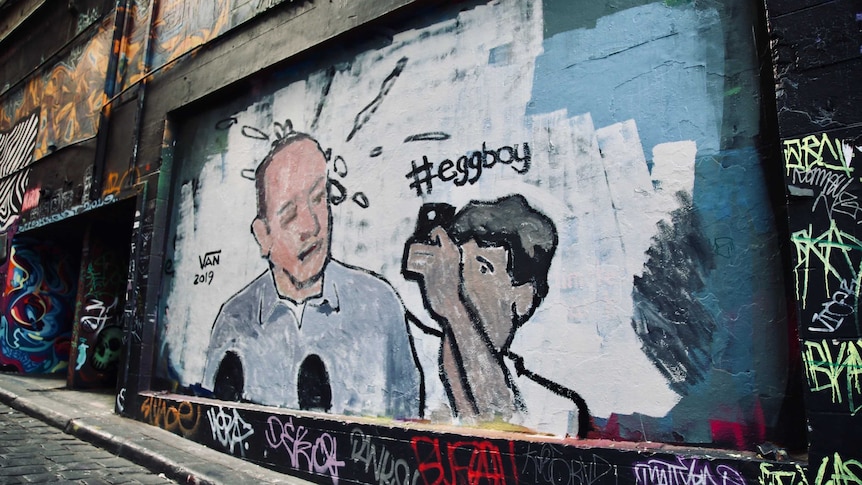 A mural depicting the egging of Senator Fraser Anning covers a wall in a narrow CBD laneway.