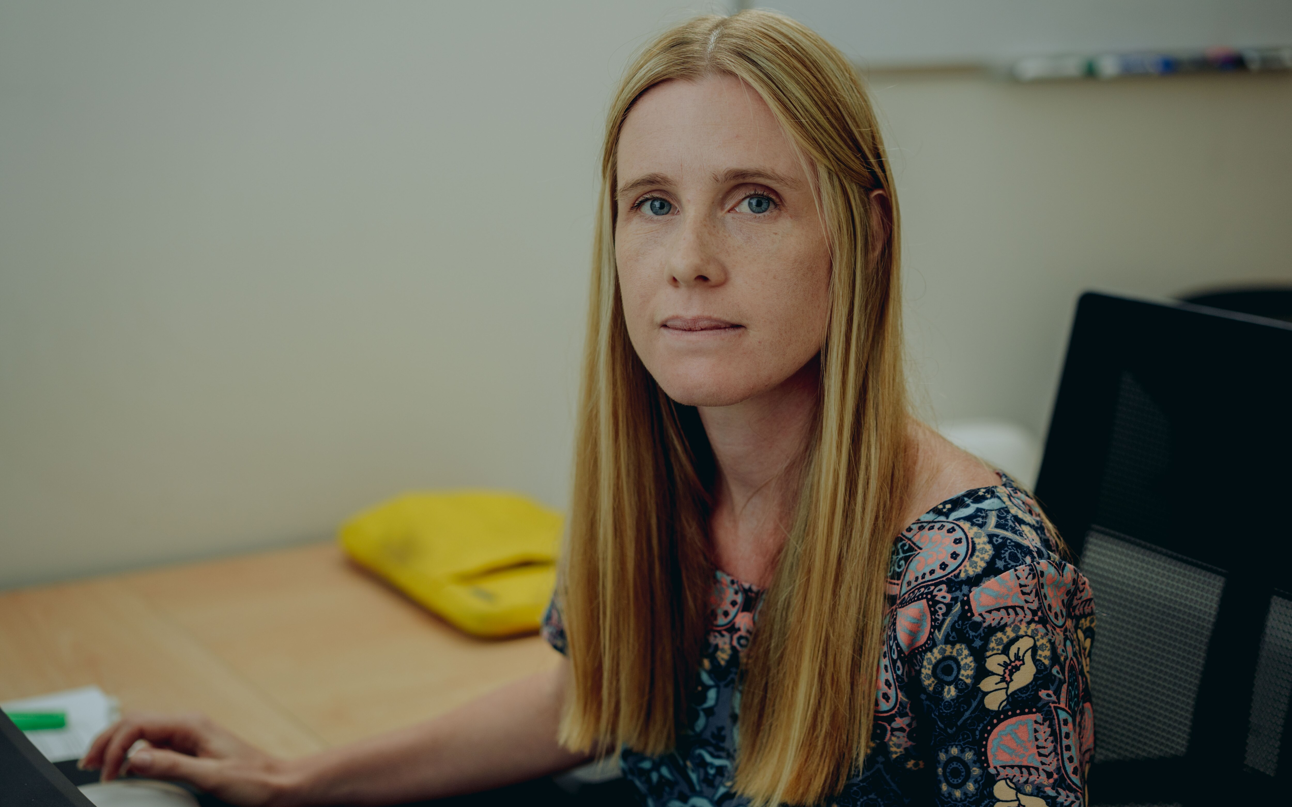a woman with long blonde hair sits at her desk looking at the camera