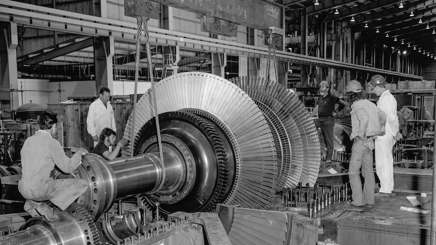 A black and white photo of several men standing around a large piece of machinery.