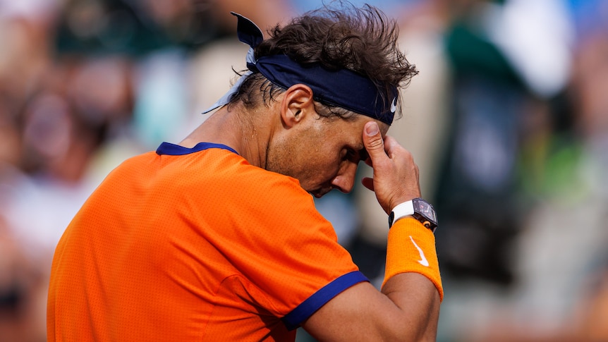 Tennis star Rafael Nadal looks down with his hand resting on his forehead during a match.