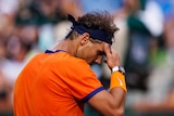 Tennis star Rafael Nadal looks down with his hand resting on his forehead during a match.