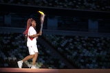 Woman with long red and black dreadlocks wears white, carries large torch