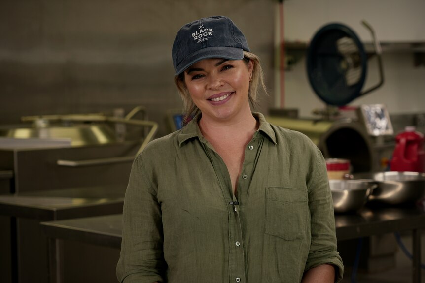 Woman wearing navy cap and green linen shirt smiles at camera. 