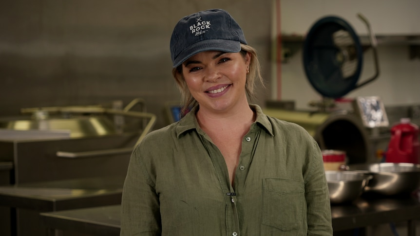 A smiling blonde woman wearing a cap and a work shirt.