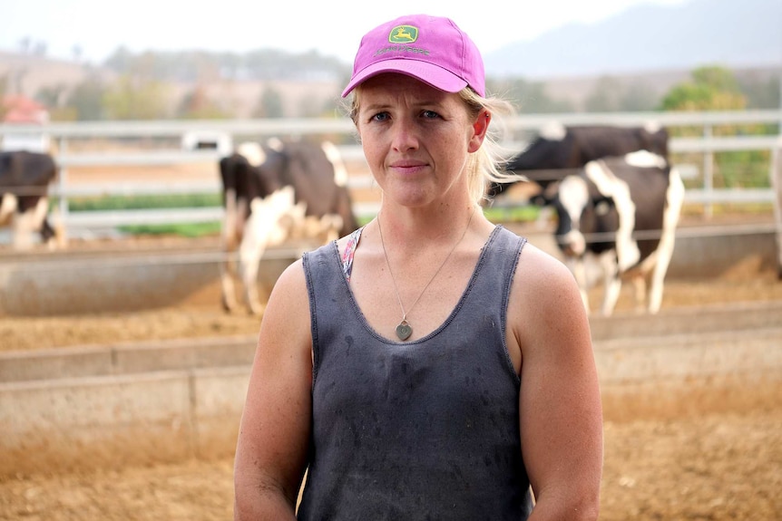 A woman in a pink hat and a blue work singlet with cows in the background