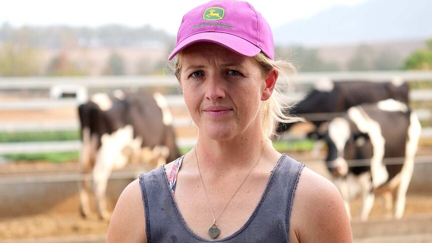 A woman in a pink hat and a blue work singlet with cows in the background