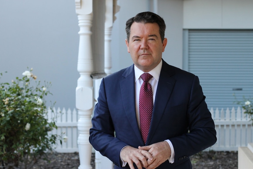 Dean Smith standing on a front verandah and wearing a suit.