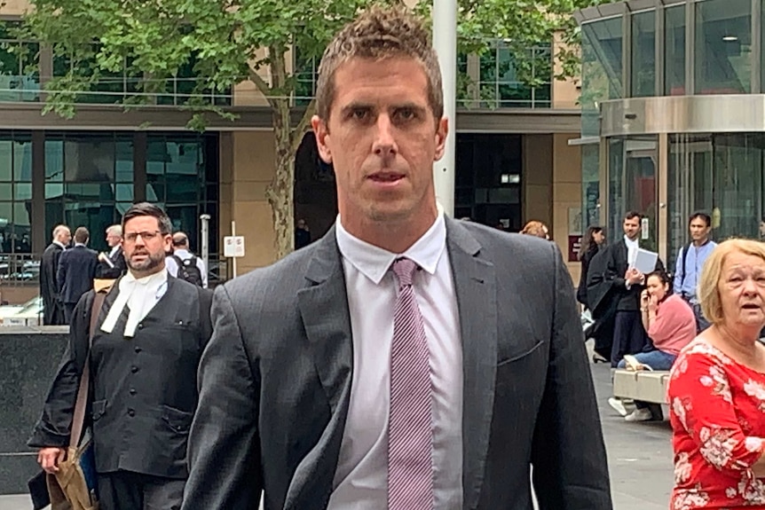 Police officer Travis Woolnough walks out of a courthouse wearing a neutral expression on his face and a suit.