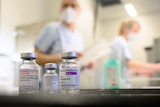 Glass vials in the foreground, masked people in background