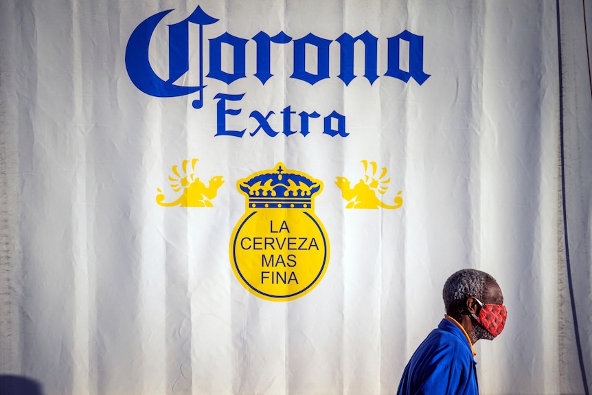 A man wearing a face mask walks past a Corona Extra beer advertisement