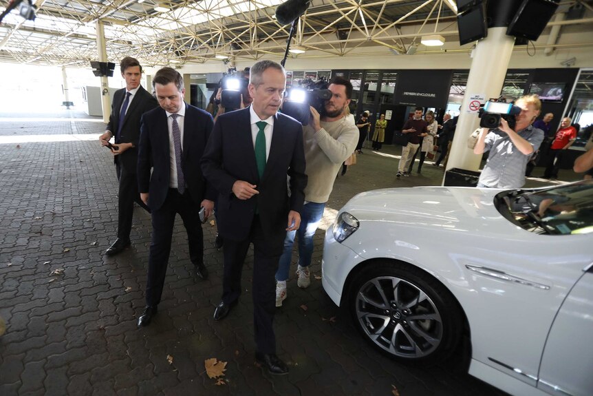 Bill Shorten and an adviser walk towards a car refusing to answer questions from journalists
