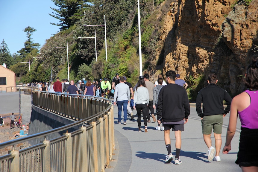 People walk down a beachfront promenade on a sunny day.