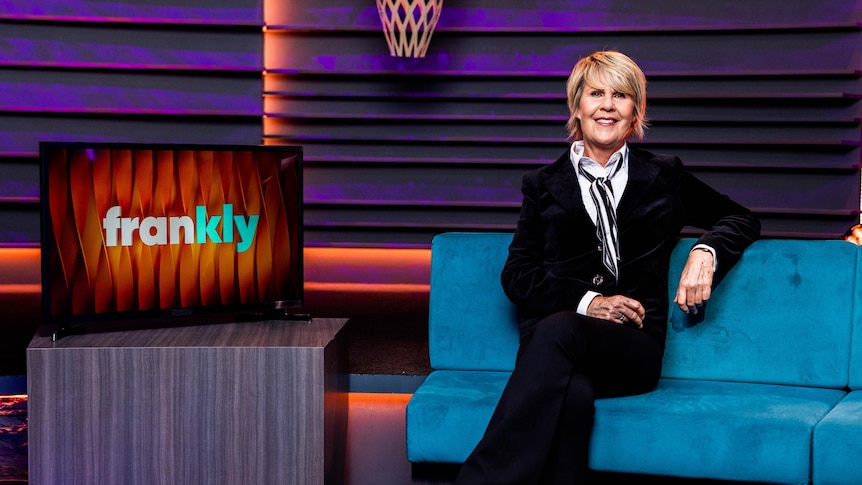 Woman sitting on a teal blue couch next to a TV screen with words frankly on it.