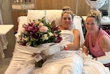 Elmarie Steenberg and Marle Swart hold flowers while in a hospital bed.