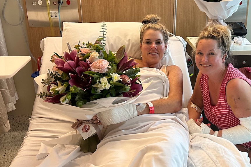 Elmarie Steenberg and Marle Swart hold flowers while in a hospital bed.