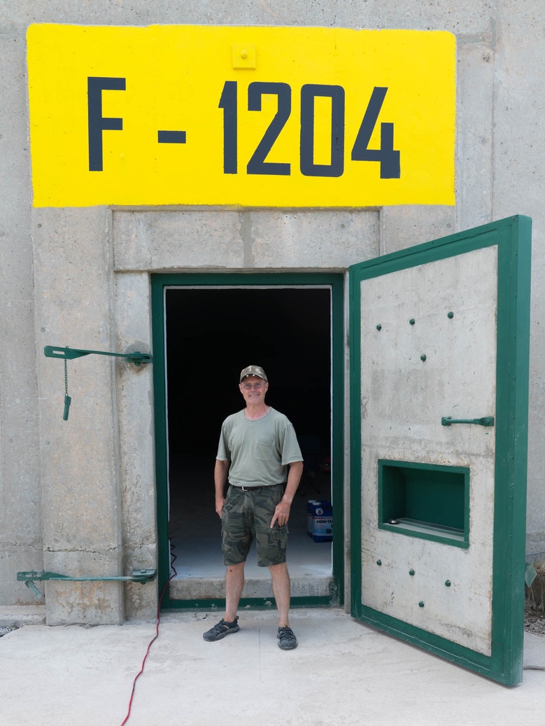 A man stands outside his concrete bunker.