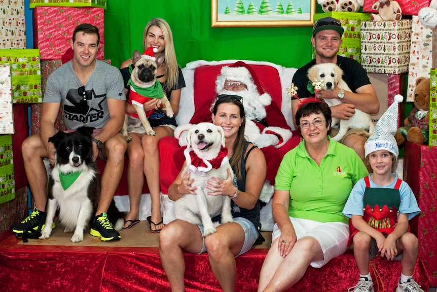 Group photo of dog owners and their pets posing for photo with Santa and his helpers