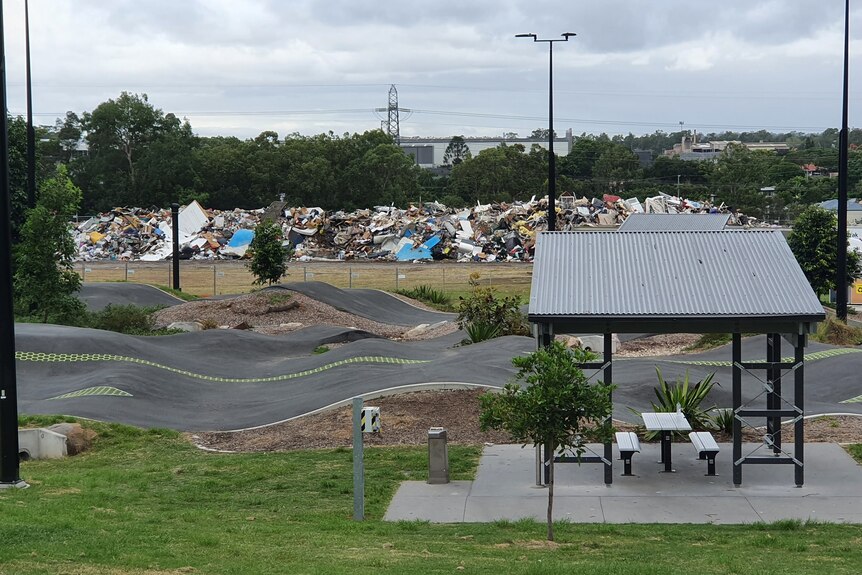 An image of a park with a bike track and pagola with piles of waste dumped in the background