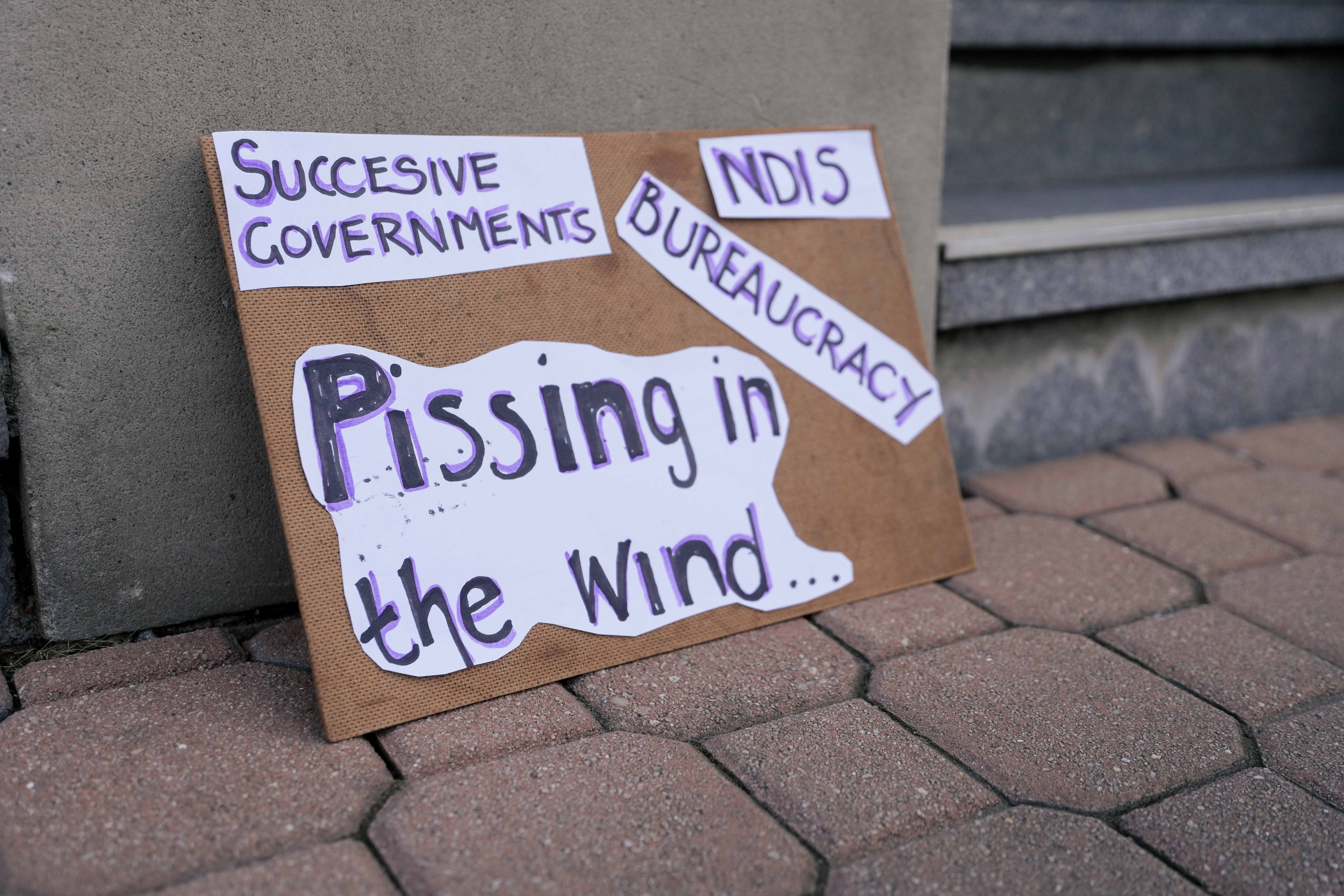 A man in a wheelchair protests with others holding signs