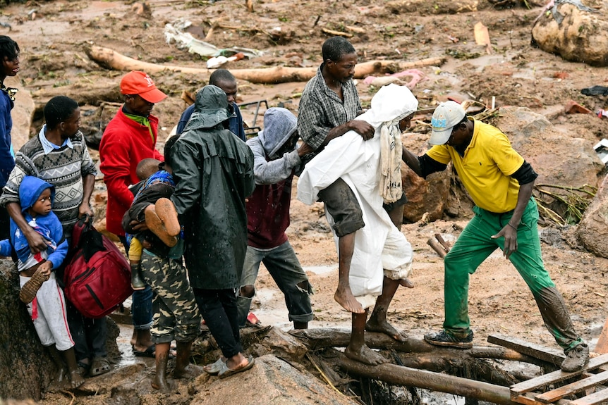 An injured man helped across wood planks after a mud slide.