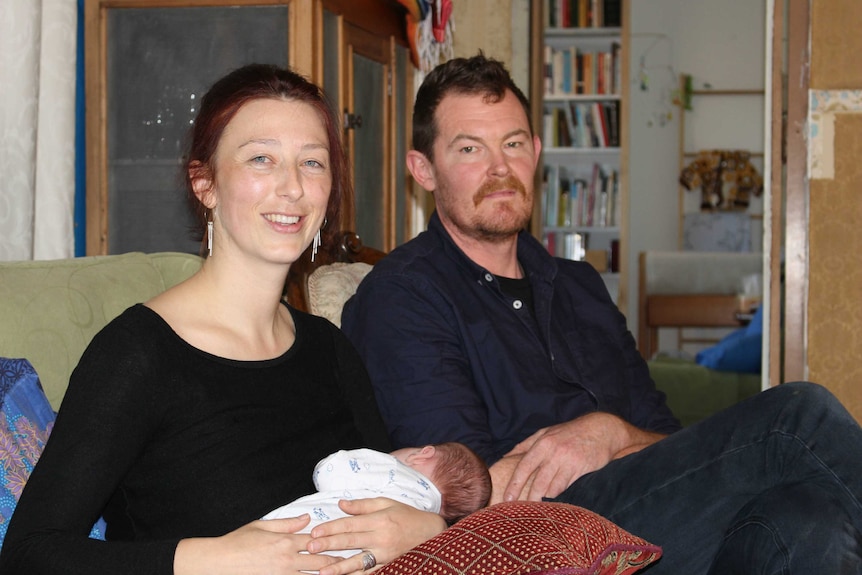 A couple sits on a couch with a small baby.