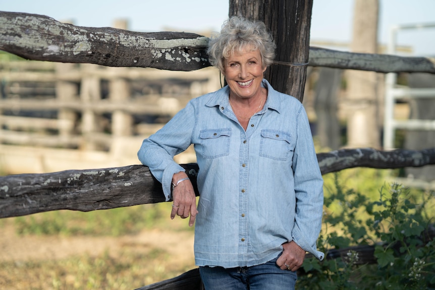 Woman standing and smiling in front of a farm fence. 