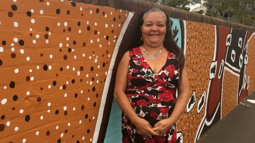 Woman stands in front of Indigenous art on a wall