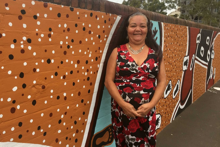 Woman stands in front of Indigenous art on a wall