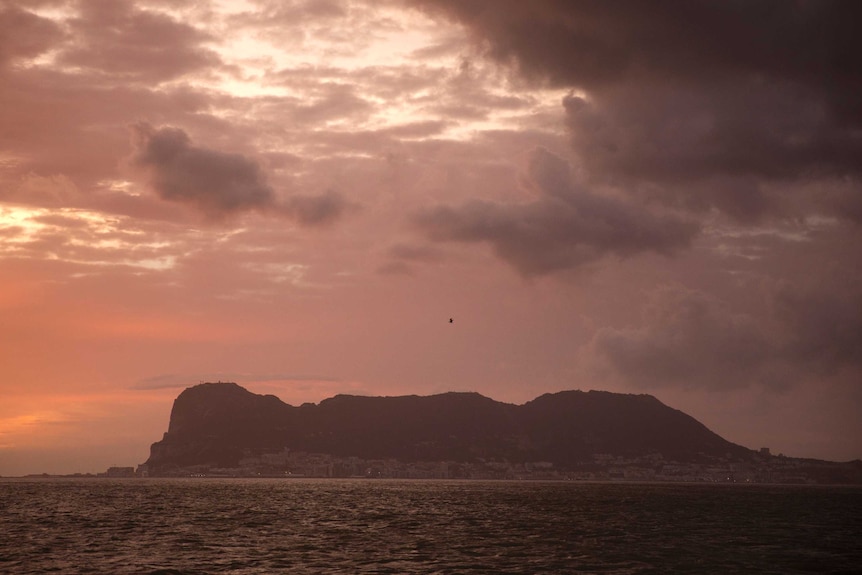 The rock of Gibraltar is seen from Spain at dusk, with an orange-hued sea in the foreground.