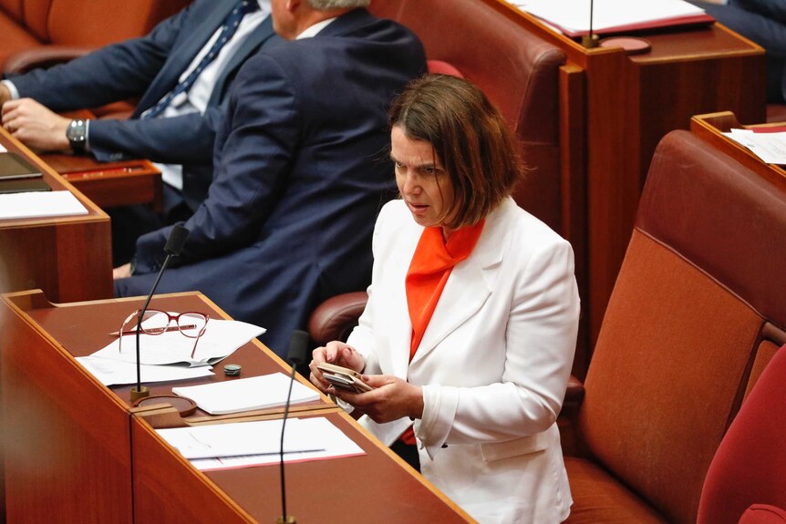 Senator Ruston looks surprised as she clutches her phone, while sitting on the frontbench.