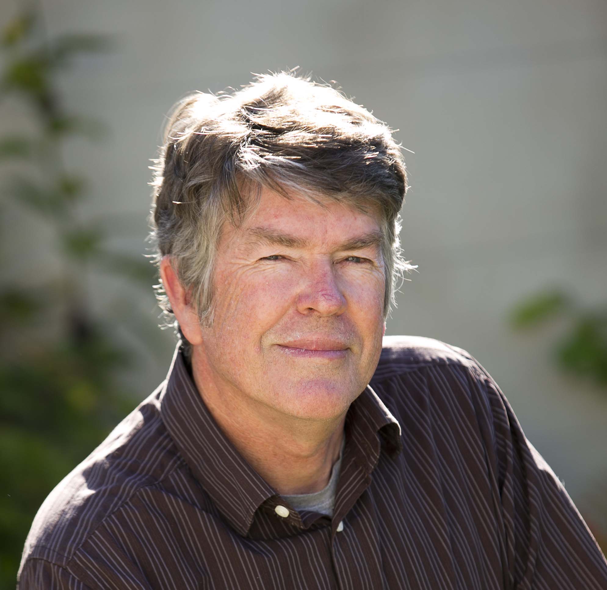 Um homem veste uma camisa escura e sorri.