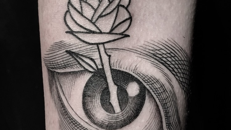 An arm with a tattoo of a rose poking through the iris of an eye