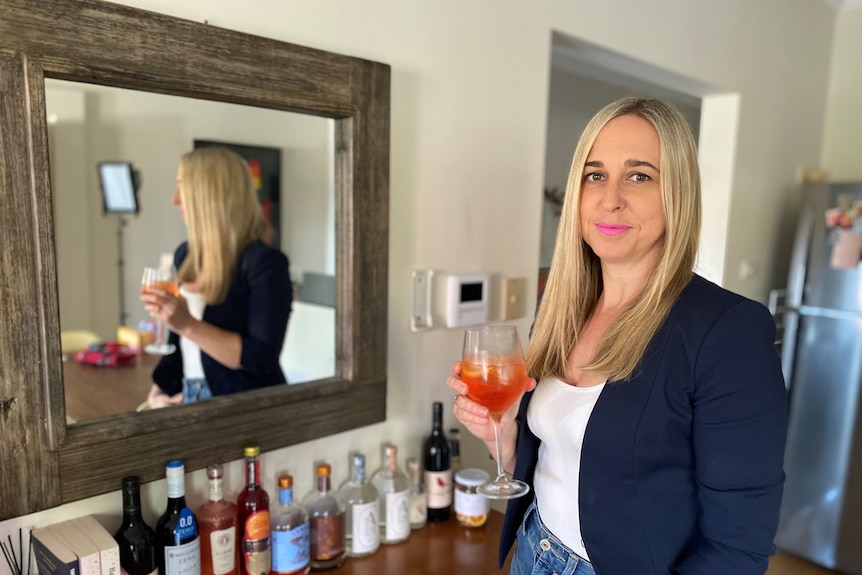 A woman standing in front of a mirror holding a non-alcoholic drink.