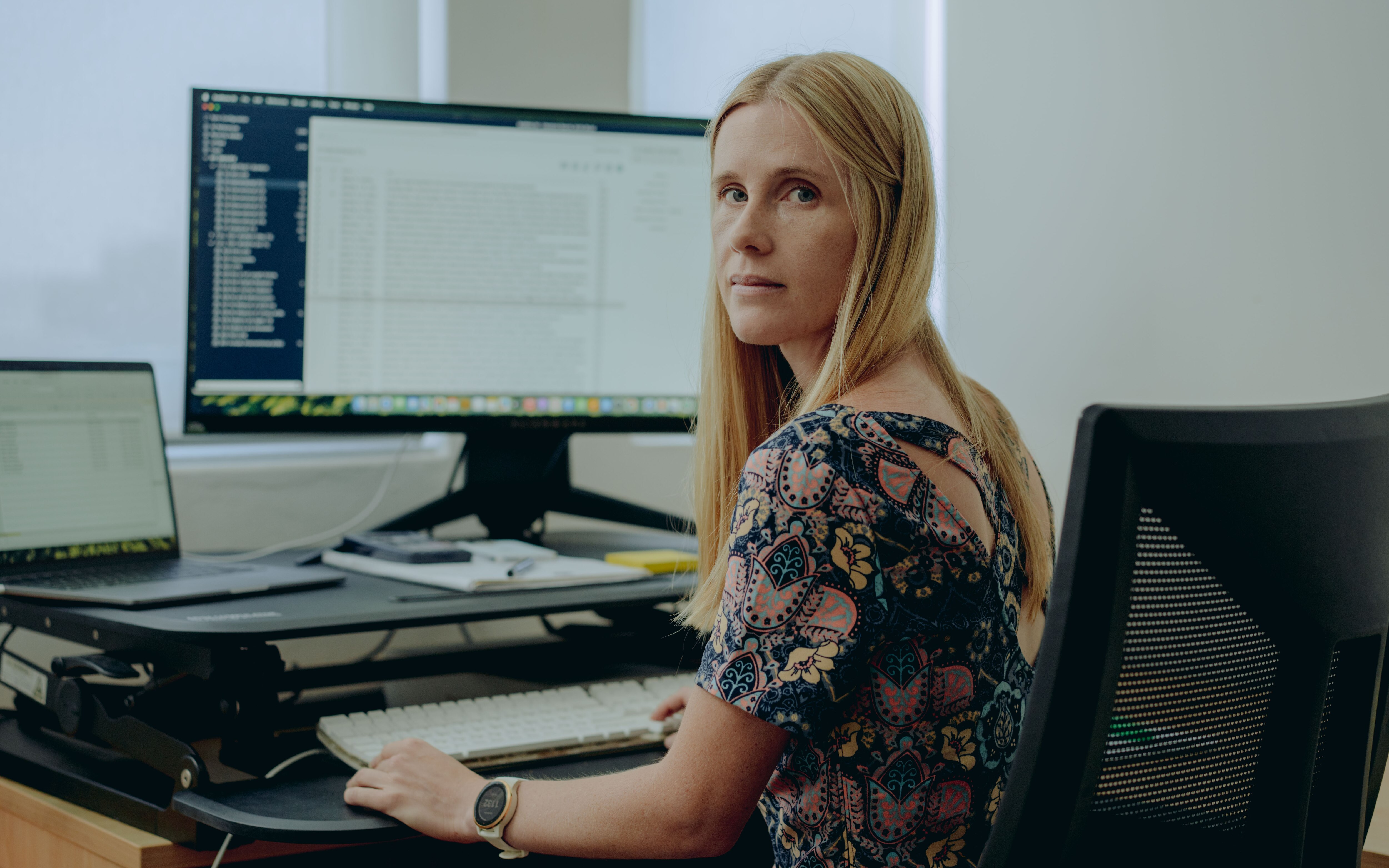 a woman with long blonde hair sits at her desk