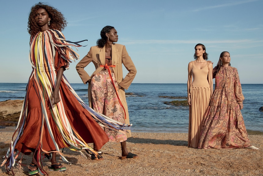 Four women pose on the beach in designer clothes