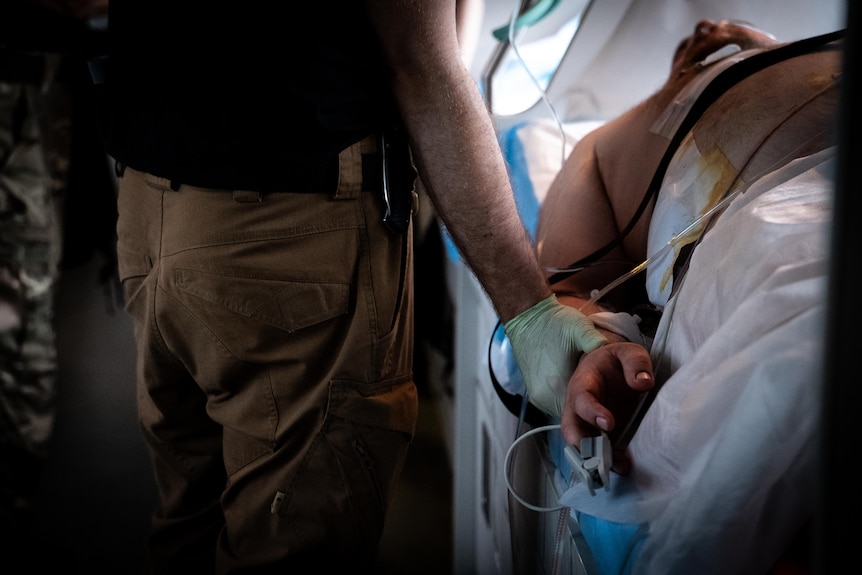 A medic wearing blue gloves grasps a patient's hand 