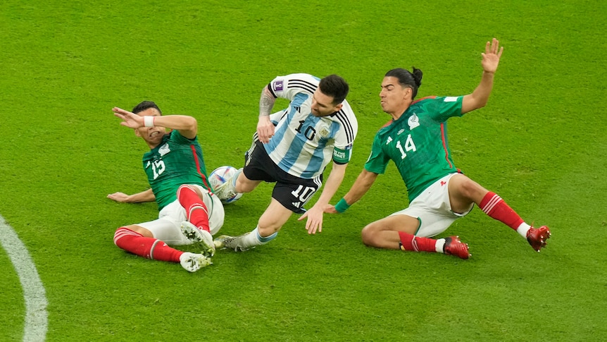 Lionel Messi falls to the ground under pressure from two tackling Mexico players