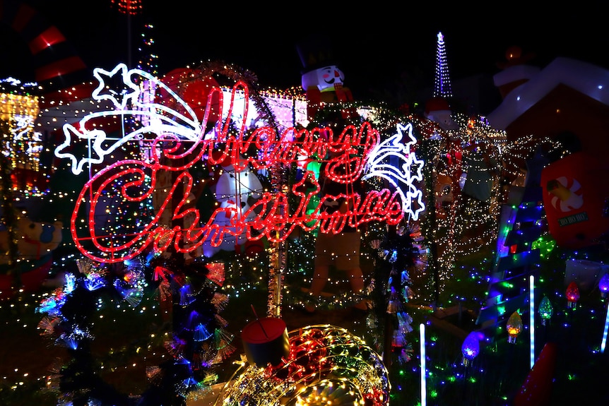 A red merry christmas sign in the foreground, it's surrounded by dozens of other lights and inflatables.