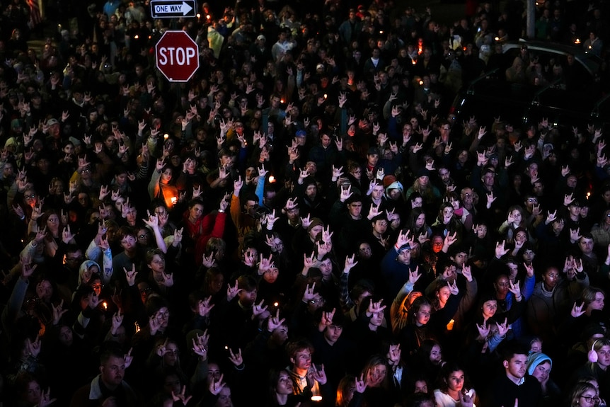A crowd of people stand together and hold up their hands to sign I love you.