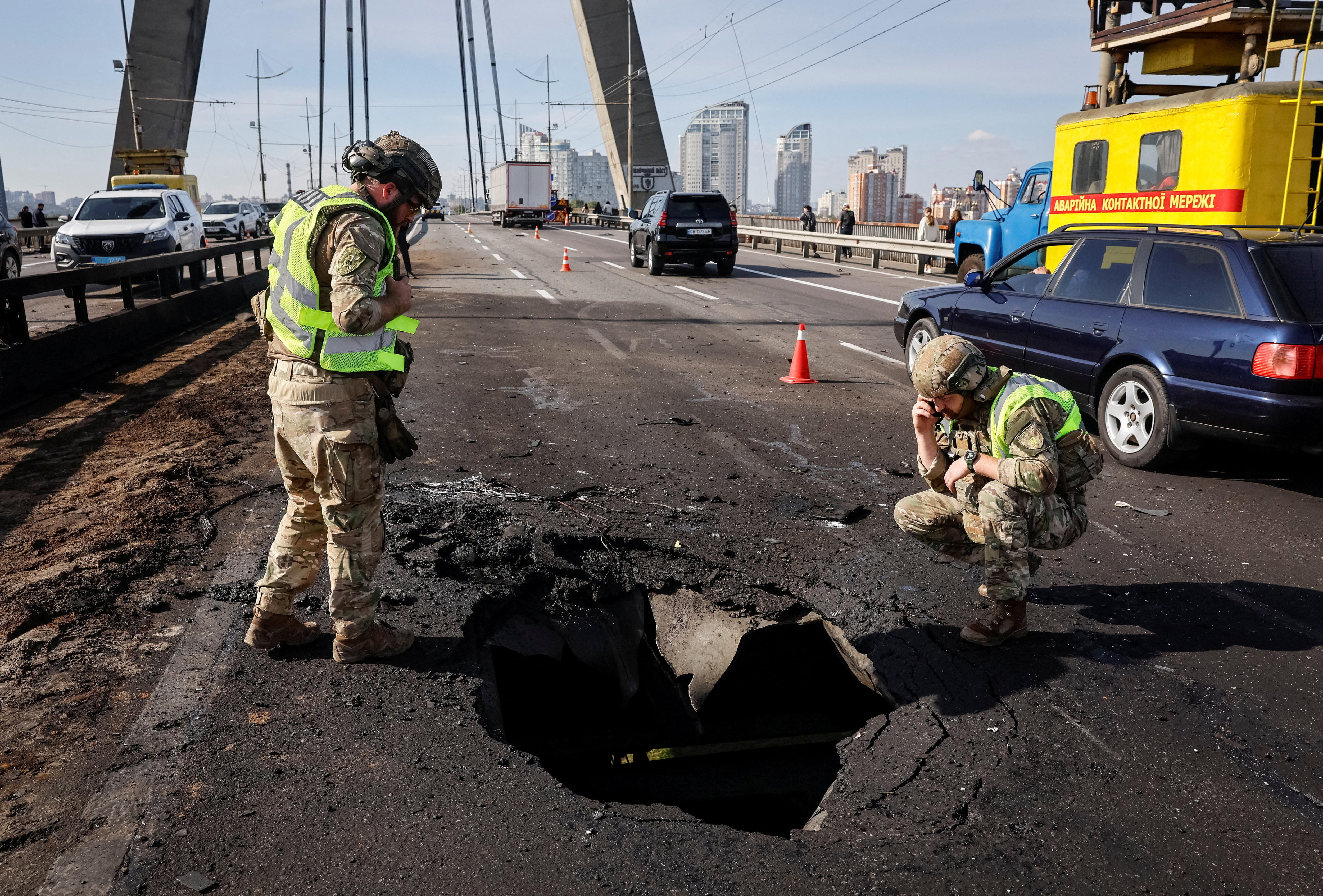 Two officers inspecting a metre-wide crater in the surface of a bridge roadway.
