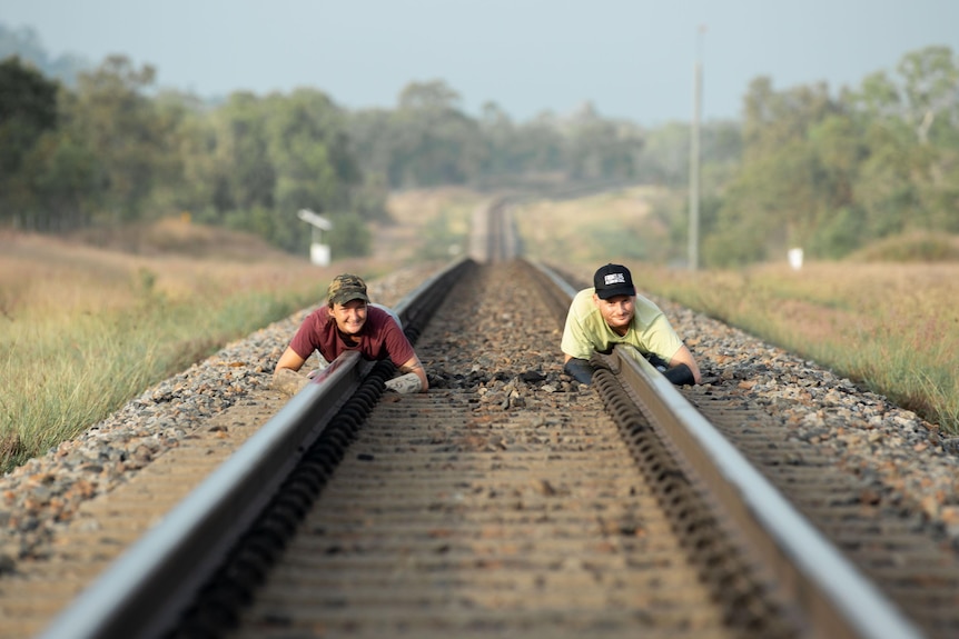 Two people lying on rail line.