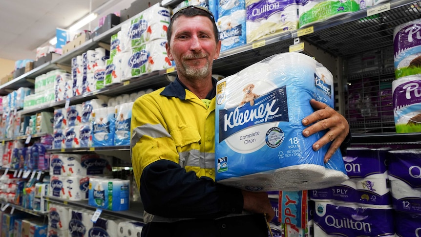 A man in a high vis shirt holds a pack of toilet paper in a supermarket aisle